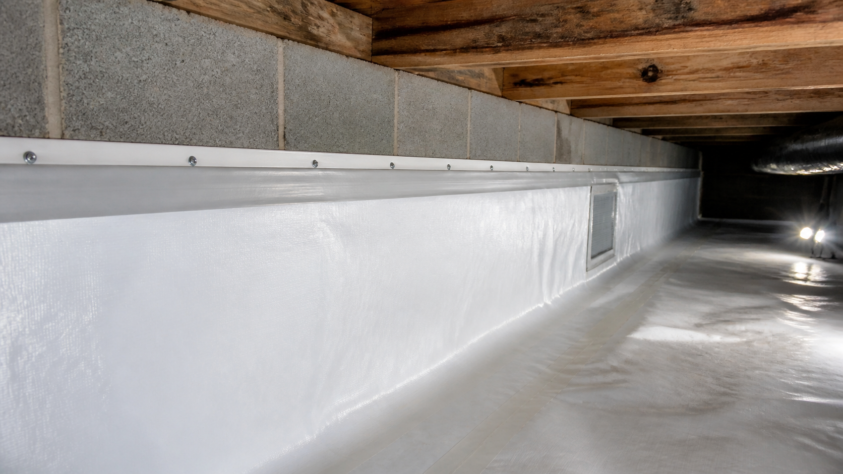 Close view of white crawl space liner running up a concrete block wall and fastened along a straight termination strip with sealed tape at the top edge